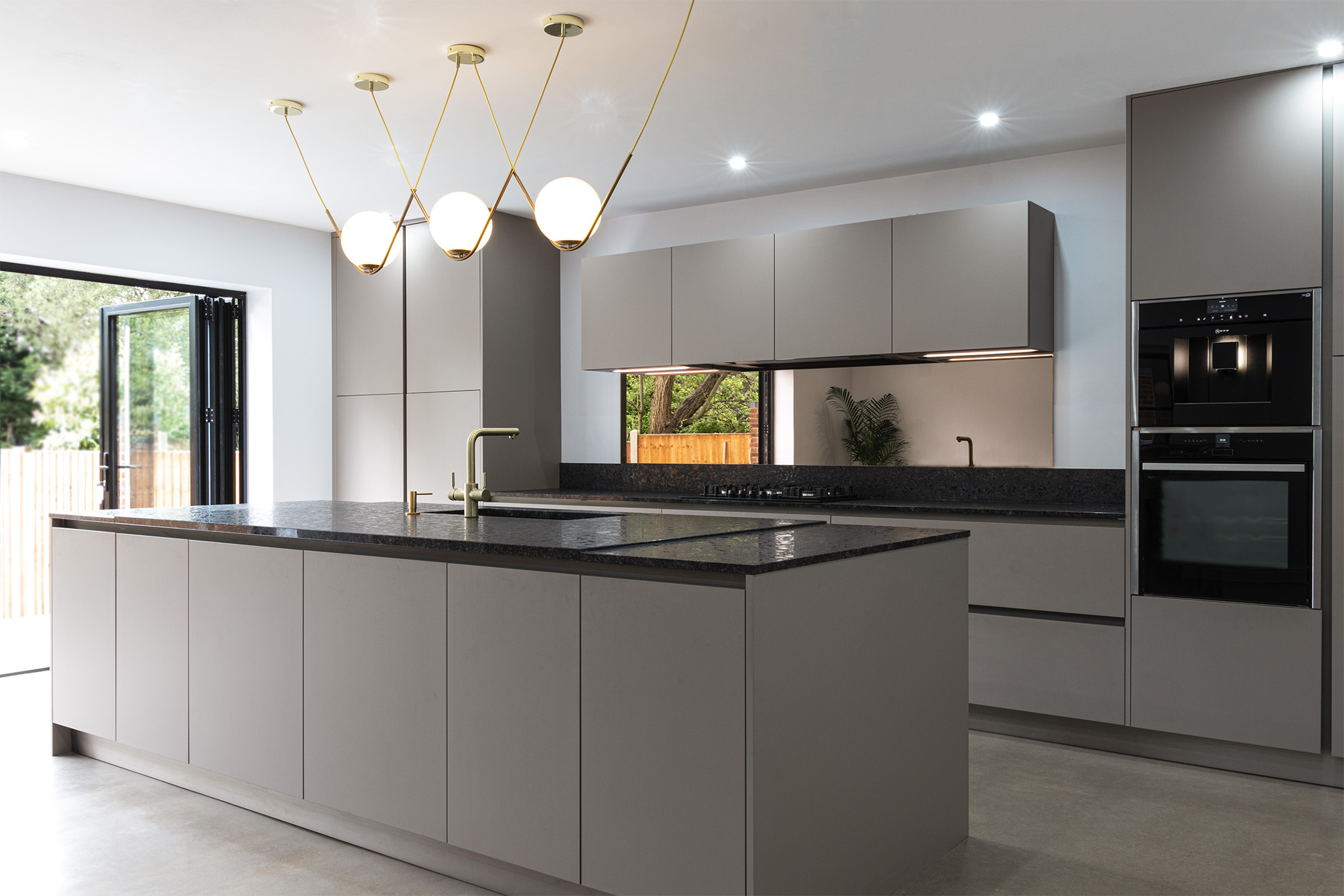 Modern kitchen in Solihull with large kitchen island, glass mirror splash back and granite with gold tap